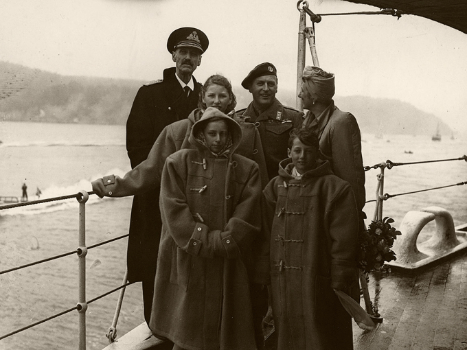 HMS Norfolk har ankommet Oslofjorden på vei hjem til et fritt Norge. Været var dårlig, så barna fikk låne varme klær av mannskapet. Foto: the Royal Navy / De kongelige samlinger